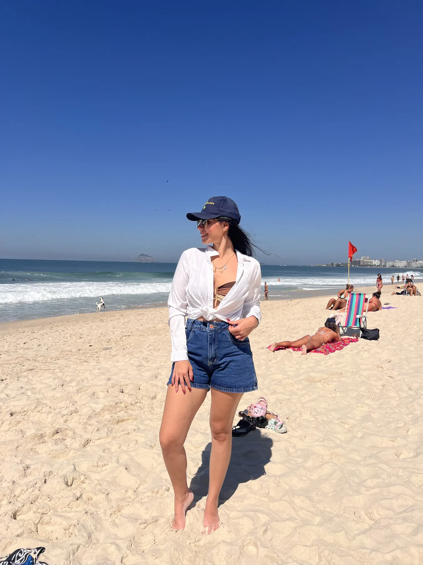 Sabrina de camisa branca e short jeans na areia da praia, em um dia de sol